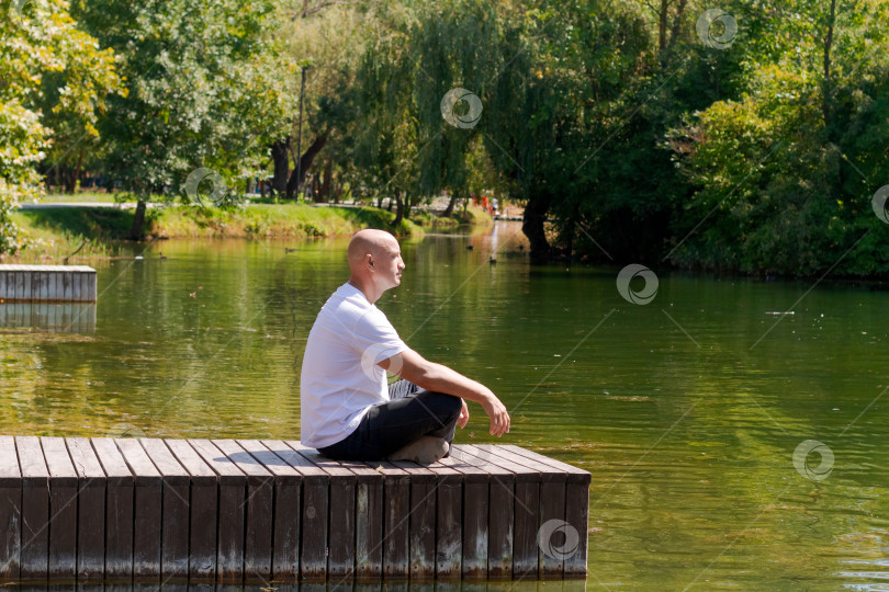 Скачать Мужчина сидит на причале у озера и смотрит на воду фотосток Ozero