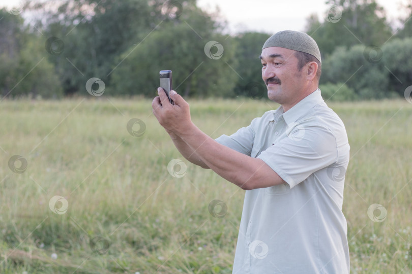 Скачать Пожилой мужчина-мусульманин фотографирует на мобильный телефон фотосток Ozero