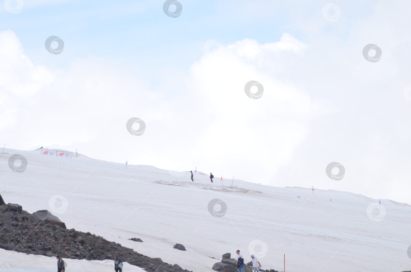 Скачать Эльбрус, Кабардино-Балкария, Россия – 07.02.2024: Горнолыжники и сноубордисты на горе Эльбрус: зимние виды спорта в августе фотосток Ozero