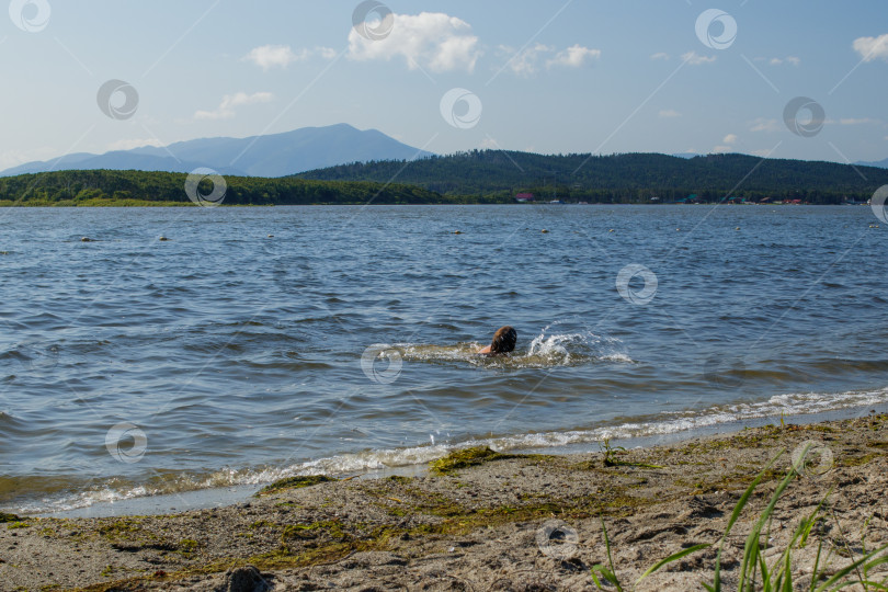 Скачать Живописное озеро Тунайча. Девушка плавает в воде у берега, поднимая брызги. фотосток Ozero