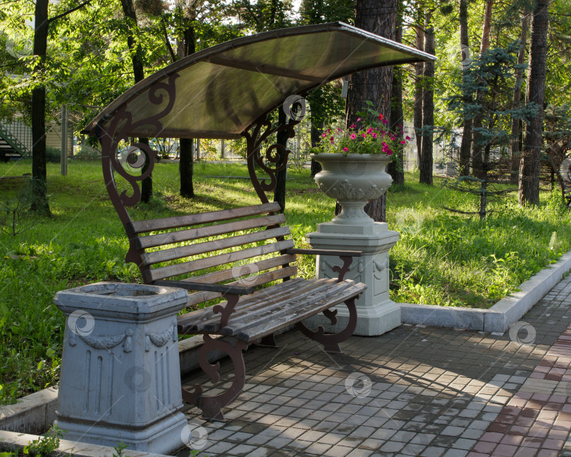 Скачать Деревянная коричневая скамейка с навесом в городском парке. фотосток Ozero