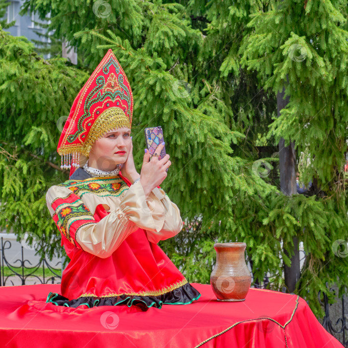 Скачать Молодая женщина в кокошнике, стилизованном под красную русскую народную одежду, пользуется смартфоном фотосток Ozero