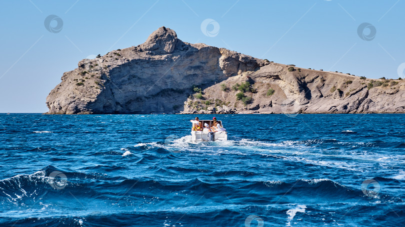 Скачать Летний морской пейзаж. Люди на лодке направляются к скале фотосток Ozero