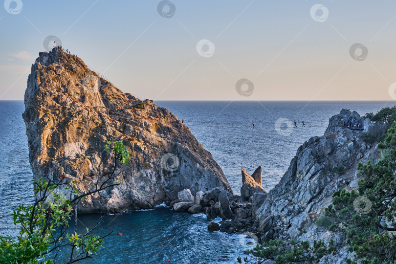 Скачать Рок-дива, побережье Черного моря недалеко от Ялты, Крым. Люди прогуливаются по подвесному мосту, поднимаются на вершину, отдыхают на пляже фотосток Ozero