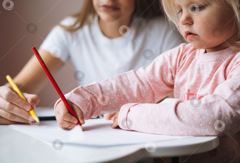 Скачать Маленькая девочка-малыш со своей мамой рисуют цветными карандашами на столе в детской комнате дома фотосток Ozero