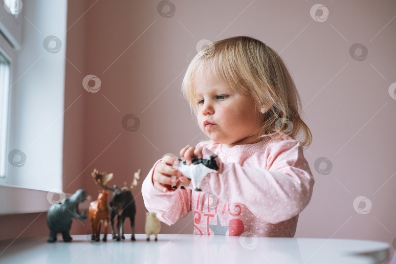 Скачать Маленькая девочка-малыш в розовом, играющая с игрушками животных на столе в детской комнате дома фотосток Ozero
