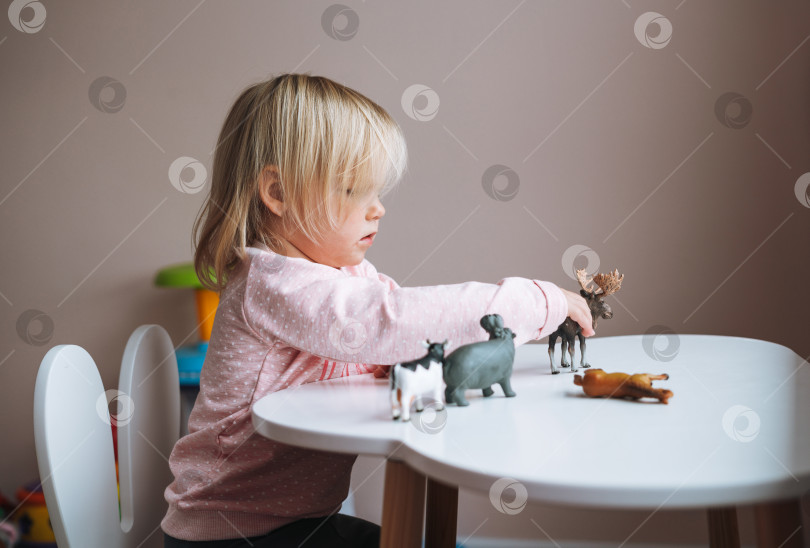 Скачать Маленькая девочка-малыш играет с игрушками животных на столе в детской комнате дома фотосток Ozero
