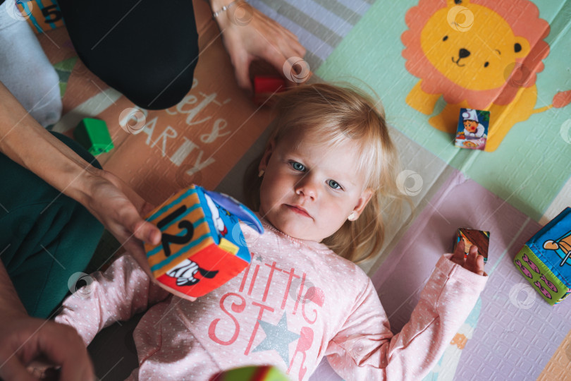 Скачать Маленькая девочка-малыш с родителями играет с кубиками с цифрами в детской комнате дома фотосток Ozero