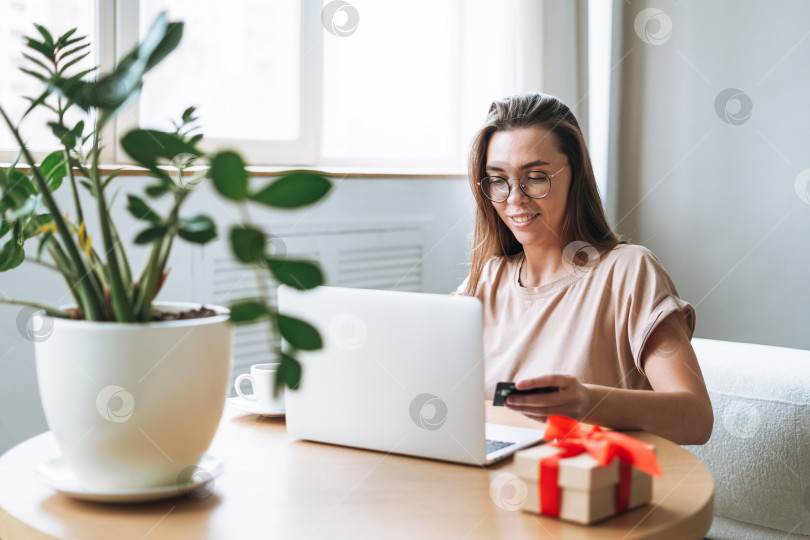Скачать Молодая женщина в очках делает покупки в Интернете на ноутбуке дома фотосток Ozero