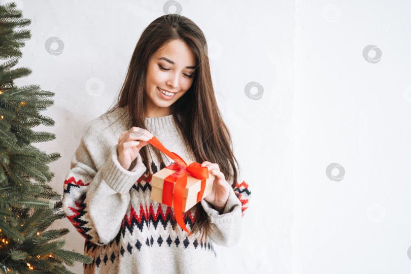 Скачать Молодая азиатка с длинными волосами с подарочной коробкой в комнате с рождественской елкой дома фотосток Ozero