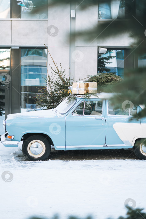 Скачать Винтажный светло-голубой автомобиль, украшенный натуральной рождественской елкой и коробками с подарками на зимней улице фотосток Ozero