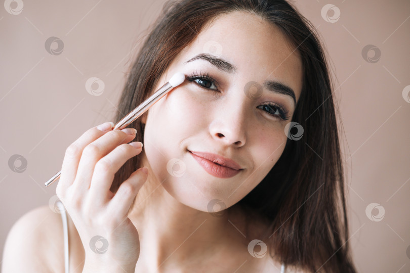Скачать Портрет молодой азиатской женщины с кисточкой для макияжа на бежевом фоне фотосток Ozero