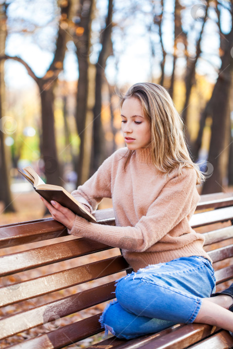 Скачать Красивая белокурая девушка с книгой сидит на скамейке в осеннем парке фотосток Ozero