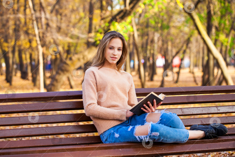 Скачать Красивая белокурая девушка с книгой сидит на скамейке в осеннем парке фотосток Ozero