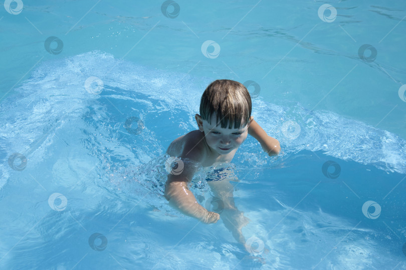 Скачать Эмоциональный малыш в бассейне играет в водные игрушки. Маленький мальчик смеется, стреляя в камеру водой из водяного пистолета. маленький мальчик 3 лет в бассейне под открытым небом с голубой водой фотосток Ozero