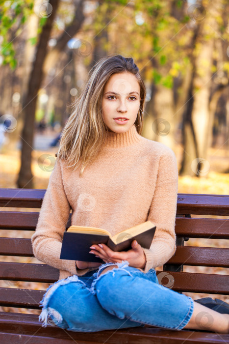 Скачать Красивая белокурая девушка с книгой сидит на скамейке в осеннем парке фотосток Ozero