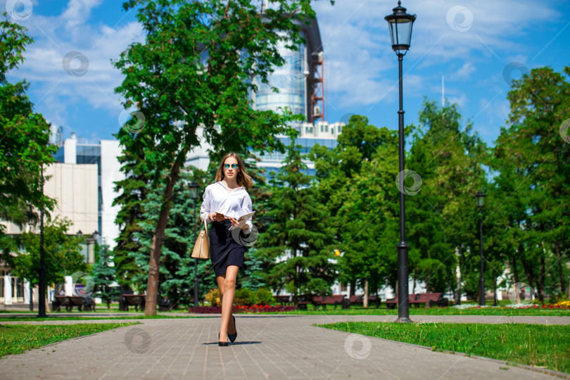 Скачать Молодая деловая блондинка прогуливается по летнему парку фотосток Ozero