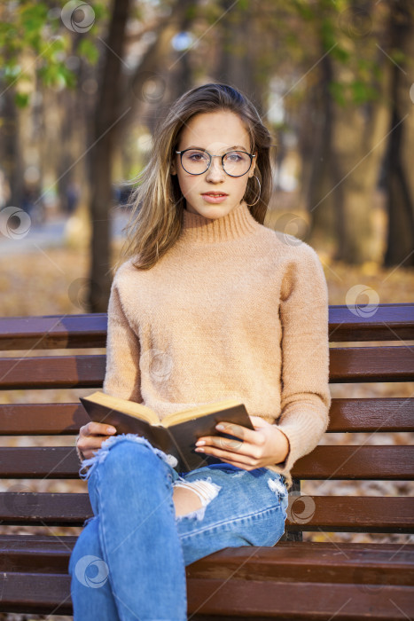 Скачать Красивая белокурая девушка с книгой сидит на скамейке в осеннем парке фотосток Ozero