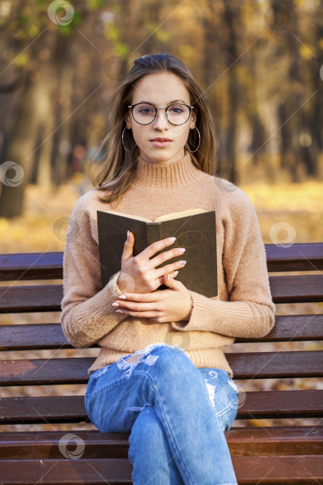 Скачать Красивая белокурая девушка с книгой сидит на скамейке в осеннем парке фотосток Ozero