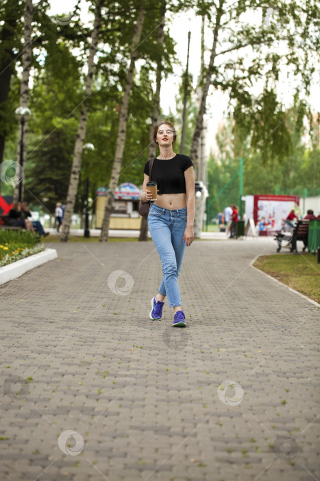 Скачать Молодая красивая брюнетка в джинсах и футболке прогуливается по летнему парку фотосток Ozero