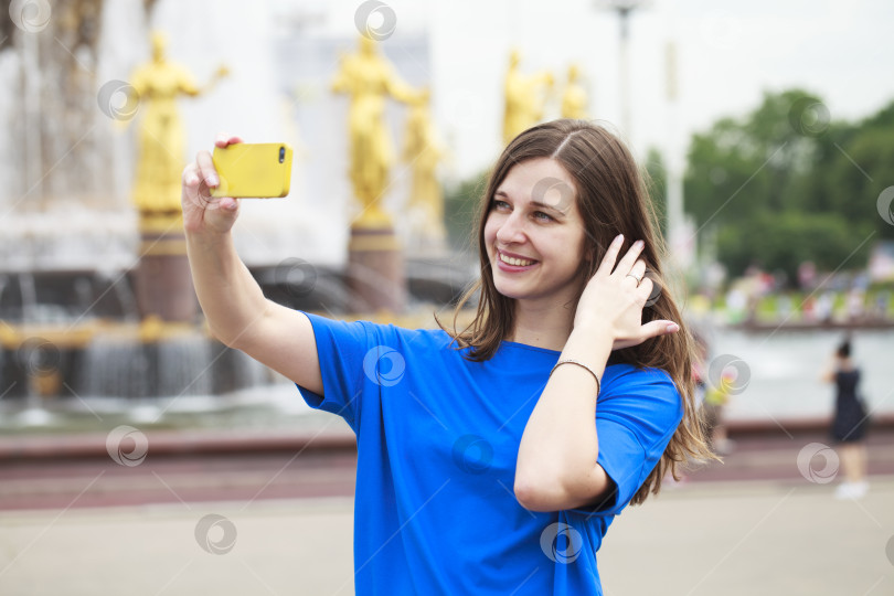 Скачать Красивая брюнетка в платье фотографирует себя на мобильный телефон в городском парке фотосток Ozero