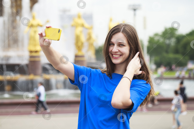 Скачать Красивая брюнетка в платье фотографирует себя на мобильный телефон в городском парке фотосток Ozero