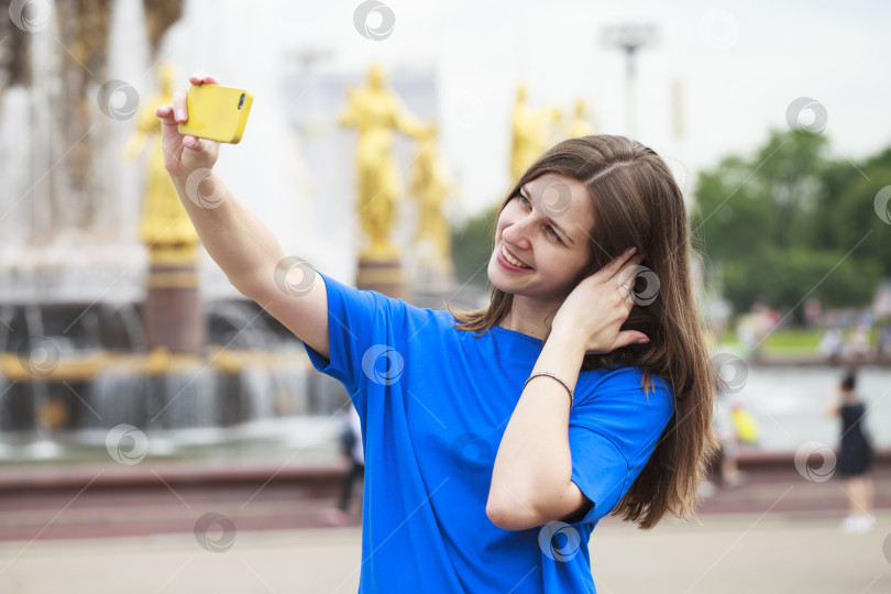 Скачать Красивая брюнетка в платье фотографирует себя на мобильный телефон в городском парке фотосток Ozero