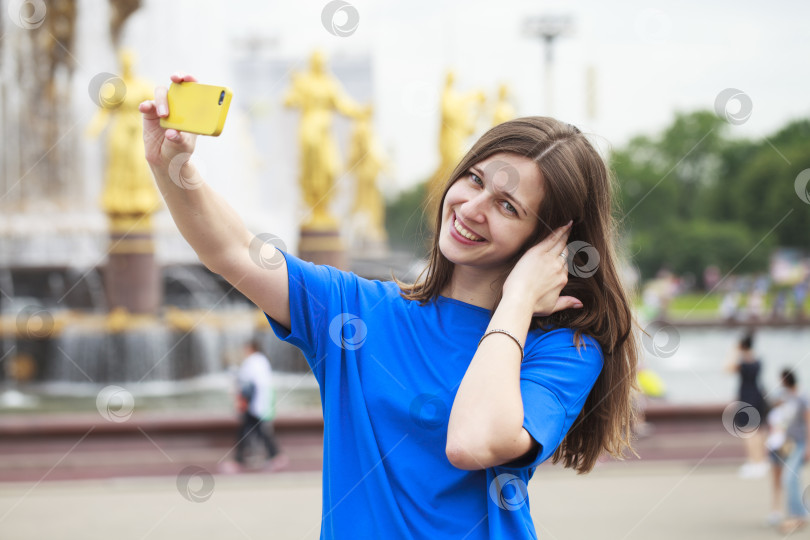 Скачать Красивая брюнетка в платье фотографирует себя на мобильный телефон в городском парке фотосток Ozero