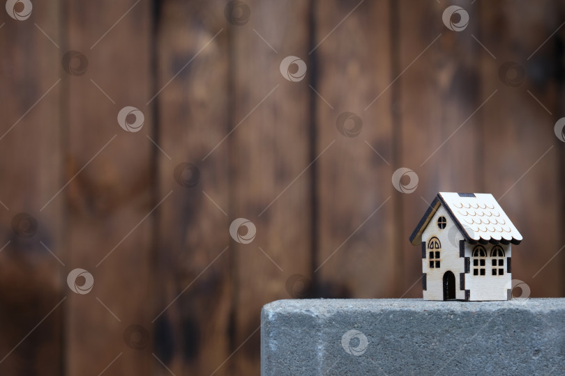 Скачать Модель деревянного дома с копировальным пространством слева на фоне деревянной стены. Дом стоит на бетонной плите, концепция строительства или покупки дома фотосток Ozero