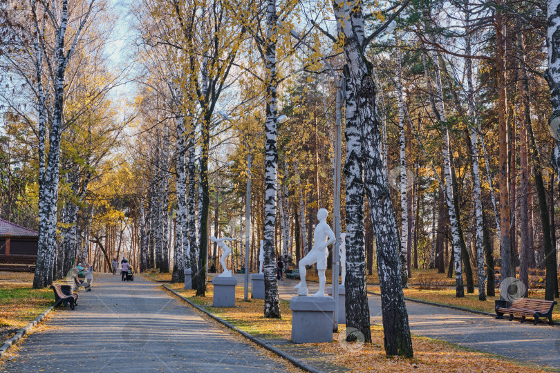 Скачать Поздней осенью люди прогуливаются по аллее городского парка. фотосток Ozero