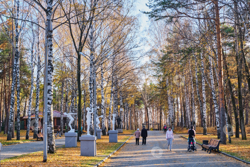 Скачать Поздней осенью люди прогуливаются по аллее городского парка. фотосток Ozero