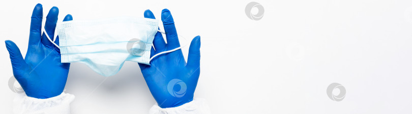Скачать Рука врача в синих медицинских перчатках держит антивирусную маску для лица на белом фоне для обозначения пандемии, воздушно-капельных заболеваний, вспышки, концепции Covid19 фотосток Ozero