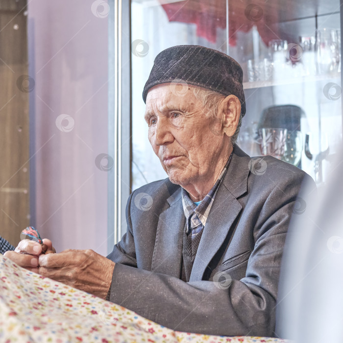 Скачать Серьезный азиат, пожилой мусульманин, сидит дома за столом фотосток Ozero