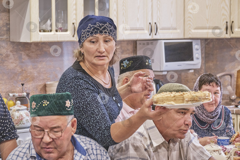 Скачать Жители сибирской деревни отмечают мусульманский праздник Курбан-байрам за домашним столом. Женщина угощает гостей медовым тортом. Ид аль-Адха фотосток Ozero