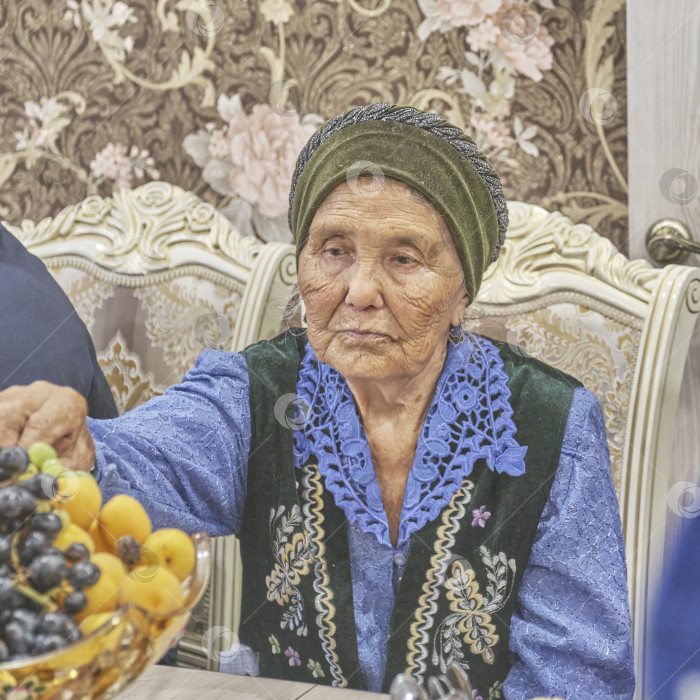 Скачать Пожилая женщина в праздничной одежде. Жители сибирской деревни отмечают мусульманский праздник Курбан-байрам за домашним столом. Ид аль-Адха фотосток Ozero