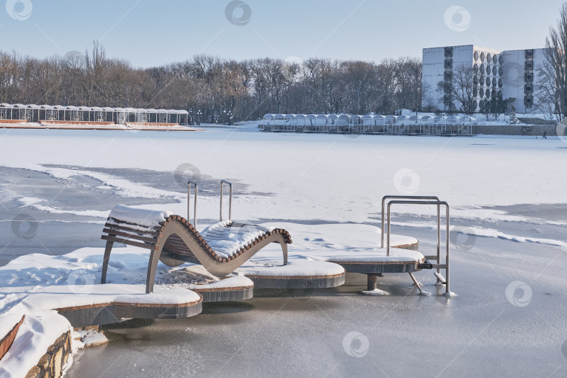 Скачать Вид на замерзшее озеро, пляж и шезлонг, покрытые снегом. фотосток Ozero