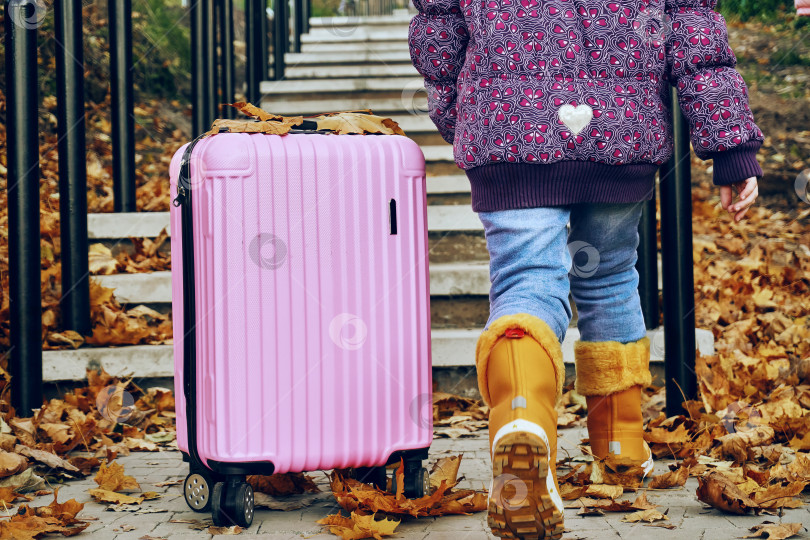 Скачать Девочка стоит на бетонной ступеньке рядом с розовым чемоданом, полным мягких игрушек, прогулка, путешествие, осень, сухие листья фотосток Ozero