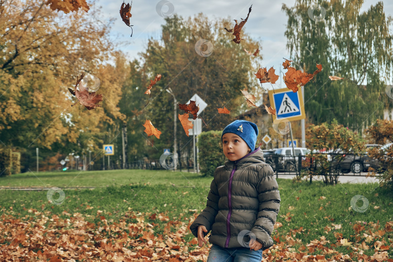 Скачать Девочка играет с сухими листьями на улице, разбрасывая их. Прогулка на свежем воздухе, осень, листья фотосток Ozero
