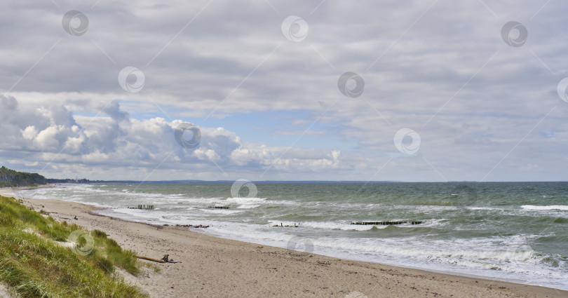 Скачать Прекрасный морской пейзаж с волнами, старым деревянным волнорезом, песчаным пляжем и облачным небом. фотосток Ozero