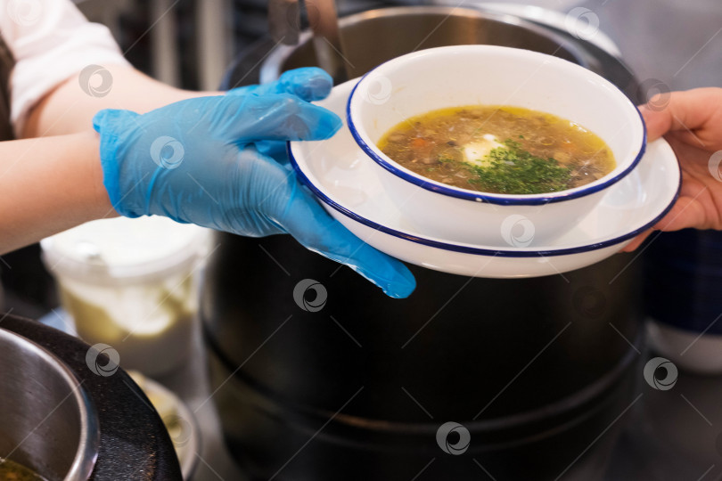 Скачать Раздача еды в столовой. Передача тарелки с супом из рук в руки на фоне горшочков. фотосток Ozero