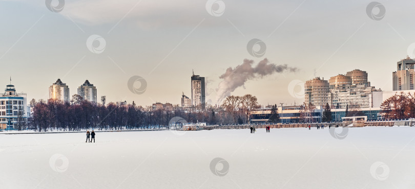 Скачать Зимний городской пейзаж Екатеринбурга, Россия. Лед городского пруда, покрытый снегом, здания, люди. фотосток Ozero