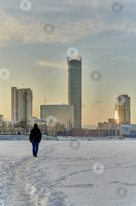 Скачать Зимний городской пейзаж. Мужчина идет по льду пруда, покрытого снегом, к берегу. Екатеринбург, Россия фотосток Ozero