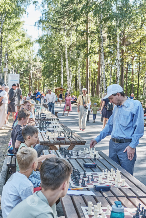 Скачать Сеанс одновременной игры в шахматы взрослого мужчины с детьми на аллее летнего городского парка фотосток Ozero