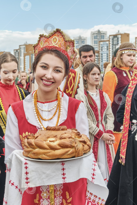 Скачать Улыбающаяся девушка в национальной русской праздничной одежде держит традиционный пирог на народном празднике Сабантуй фотосток Ozero