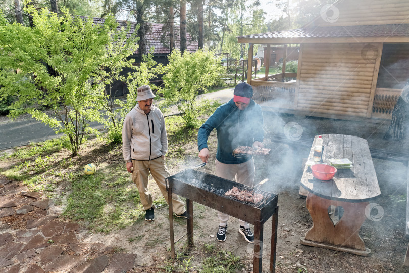 Скачать Пожилой азиат и его взрослый сын готовят мясо на гриле для барбекю на заднем дворе. фотосток Ozero