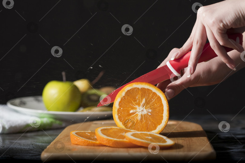 Скачать Кухонный нож для фруктов и овощей. Женские руки режут свежий апельсин фотосток Ozero
