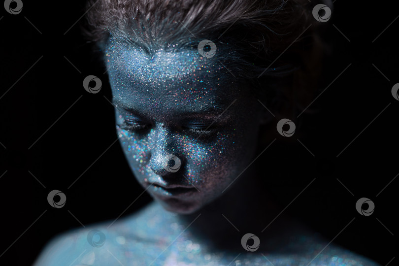 Скачать девушка с синим лицом в профиль в блестках крупным планом на черной стене смотрит вниз фотосток Ozero