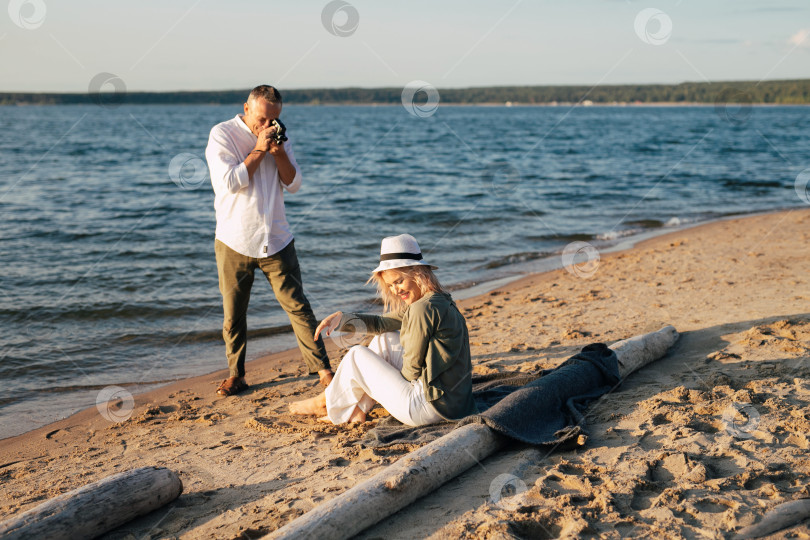 Скачать мужчина на пляже фотографирует на камеру женщину, которая сидит на пледе на песке фотосток Ozero