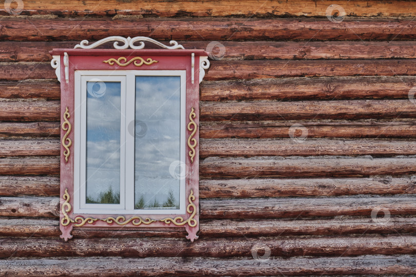 Скачать Окно с резными деревянными наличниками. Бревенчатый фасад типичного сельского дома в Бурятии, Россия. фотосток Ozero