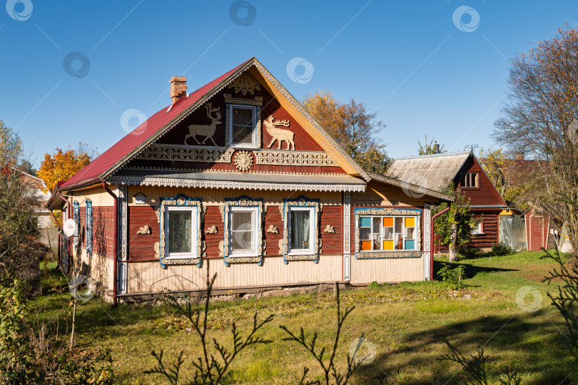 Скачать Уютный деревенский дом с ярким декором домовой резьбы среди зелени в осенний день фотосток Ozero